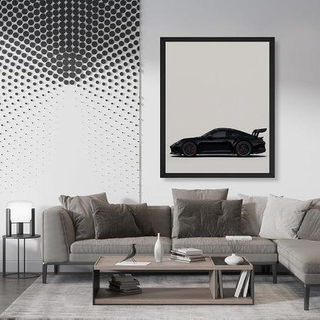 A framed art print of a black sports car on a light background, displayed on a wall in a modern living room setting above a gray sectional sofa.