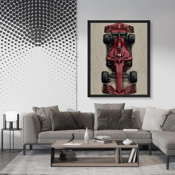 A framed vertical art print of a red Formula 1 race car on a textured beige background, displayed on a white wall above a modern gray sectional sofa in a styled living room.