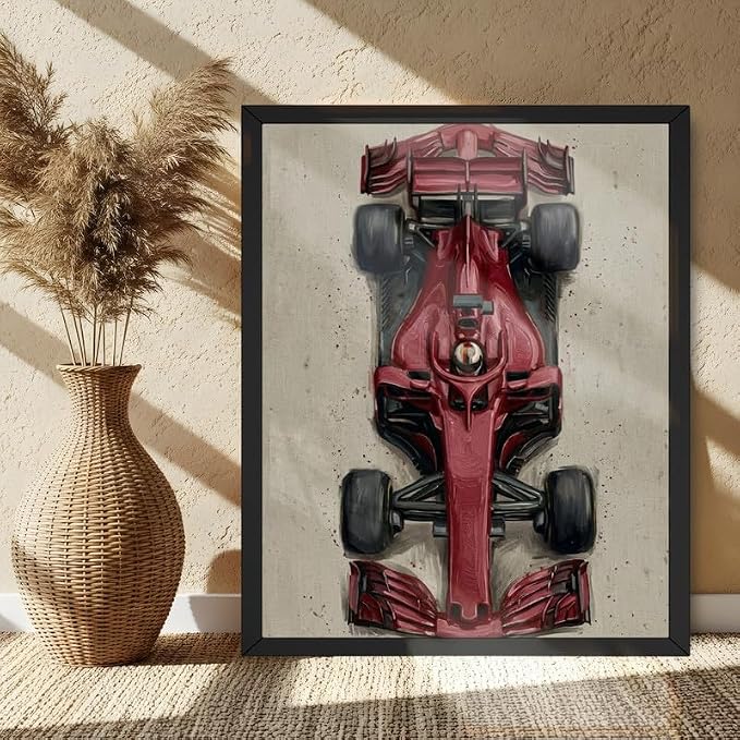 A framed art print of a red Formula 1 race car, displayed on a textured floor next to a woven vase with dried pampas grass in a sunlit room.