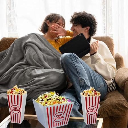 Couple enjoying a cozy movie night with popcorn bins and fleece blanket